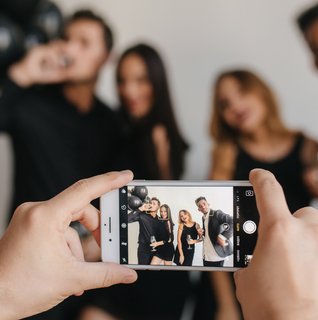 Guests taking candid photos together during a wedding or celebration while someone snaps a group picture on a smartphone, highlighting the kind of real-time guest memories couples can easily collect and share through a wedding QR code experience.
