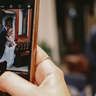Guest photographing a newlywed couple on a smartphone, illustrating how couples can collect candid wedding photos and videos through QR code photo sharing.