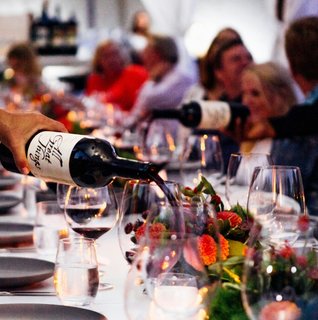 Server pours red wine at a long rehearsal dinner table decorated with colorful floral centerpieces as wedding guests gather to celebrate before the wedding day.